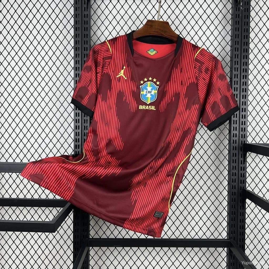 Maillot du Brésil rouge feu sur cintre, base bordeaux à rayures rouges, col noir et passepoils jaunes