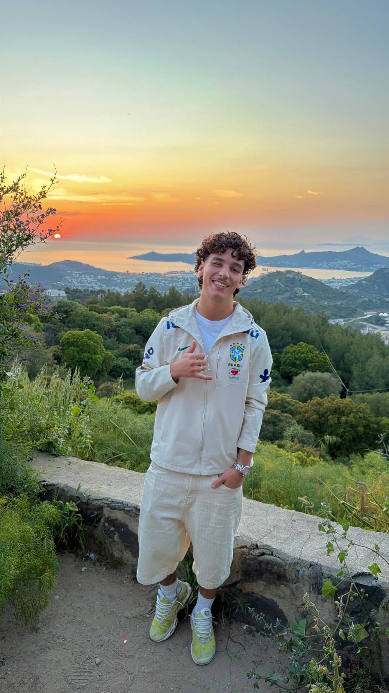 Homme souriant en veste du Brésil beige et bermuda écru, coucher de soleil sur la baie