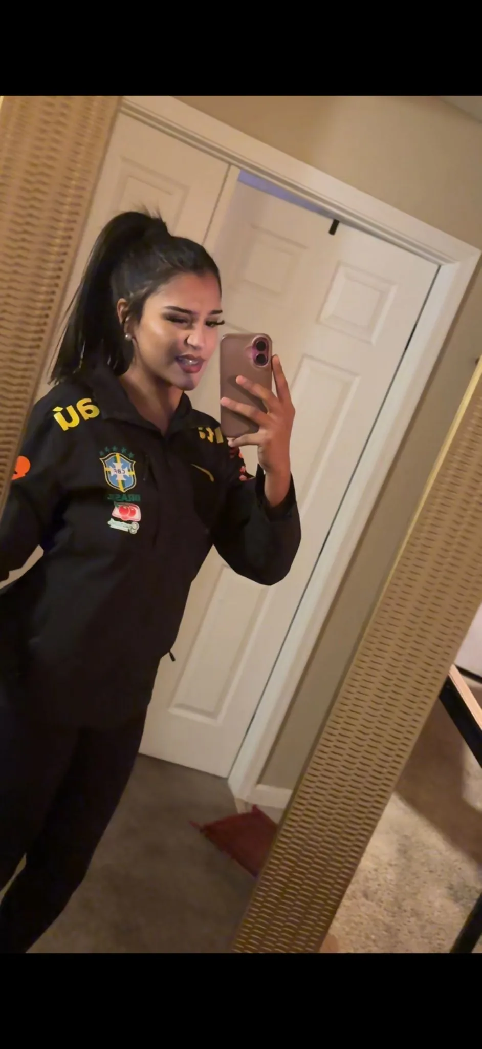 Veste du Brésil noire portée près du corps, zip fermé et écusson sur la poitrine, photographiée dans un miroir